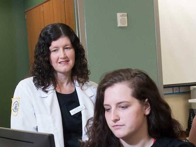 Student focusing on laptop while teacher observes student